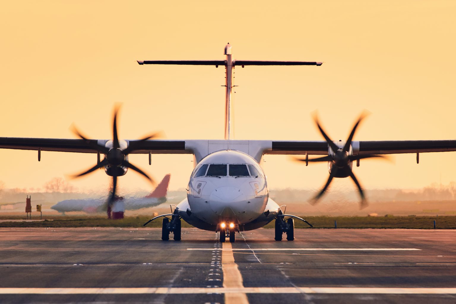 Front view of propeller airplane taxiing to runway for take off. Traffic at airpot at sunset.